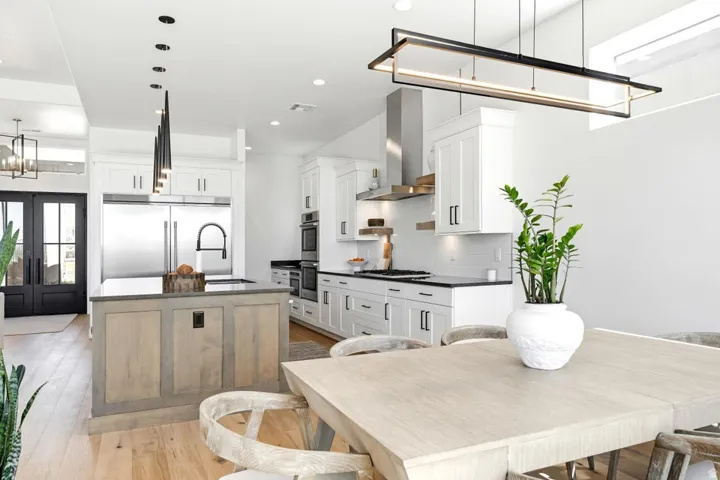Open-concept kitchen featuring an oversized island with a dark countertop, white shaker cabinetry, stainless steel appliances, and wood-finish flooring