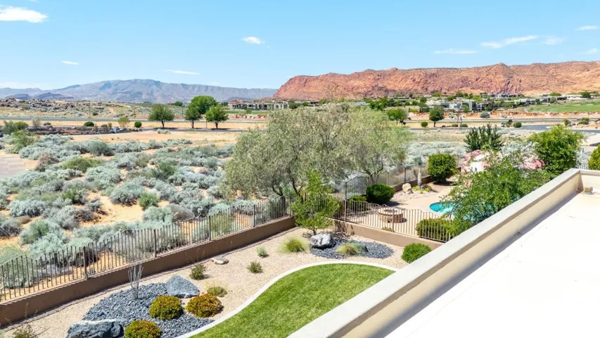 Expansive outdoor living area featuring a swimming pool, a fenced-in patio with a fire pit, and a meticulously landscaped yard with a blend of natural rock, desert plantings, and green lawn
