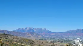 Expansive mountain ranges under a clear blue sky, featuring distant snow-capped peaks and scattered autumnal foliage