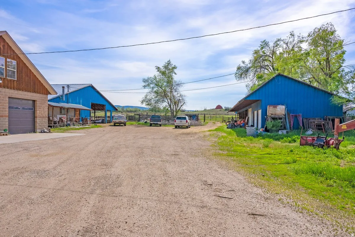 Spacious gravel driveway with multiple structures, including two blue metal-sided barns and a beige brick and wood-sided building with a garage door