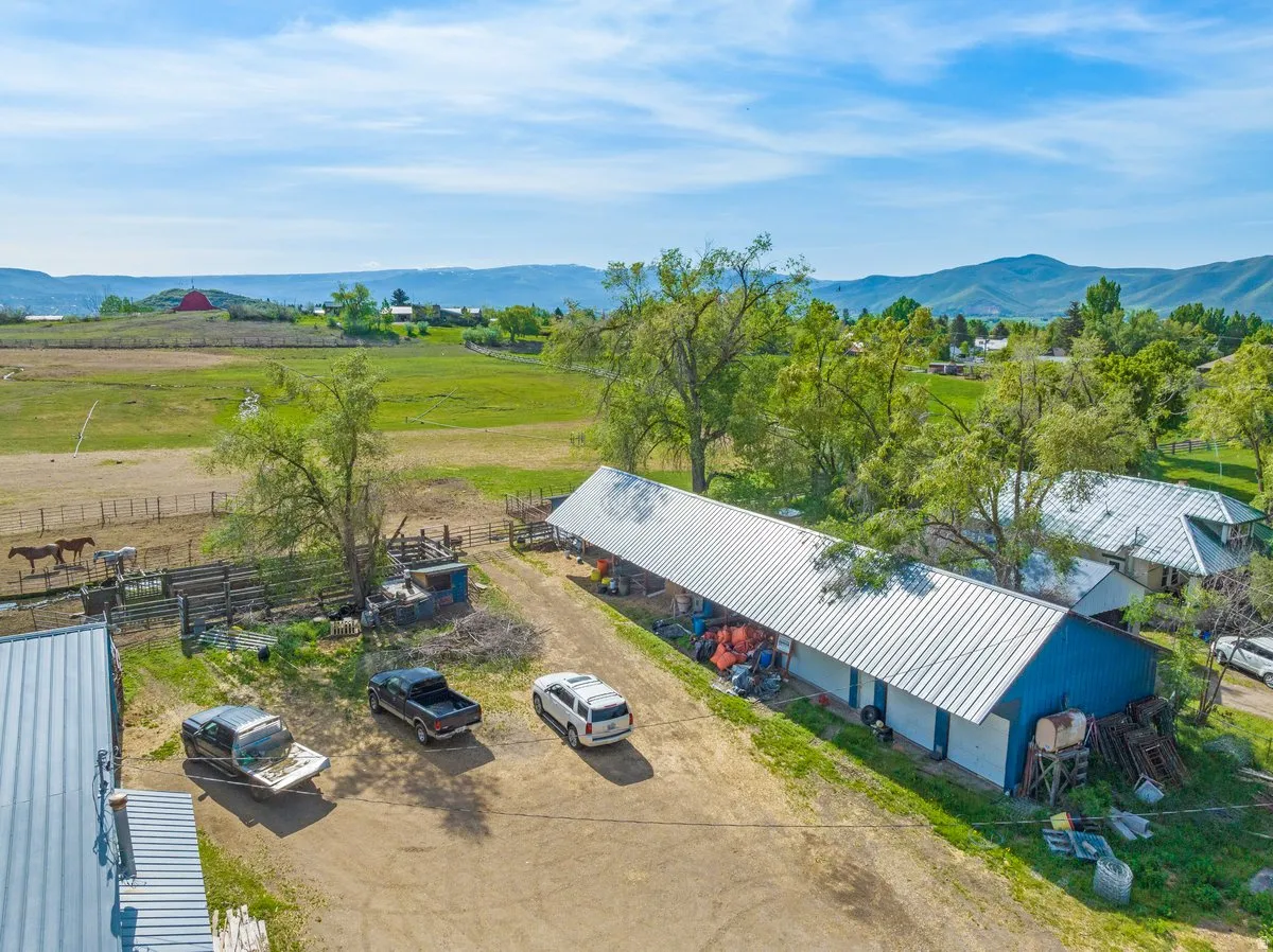 Expansive rural property featuring multiple outbuildings with metal roofs, fenced paddock areas, and abundant mature trees