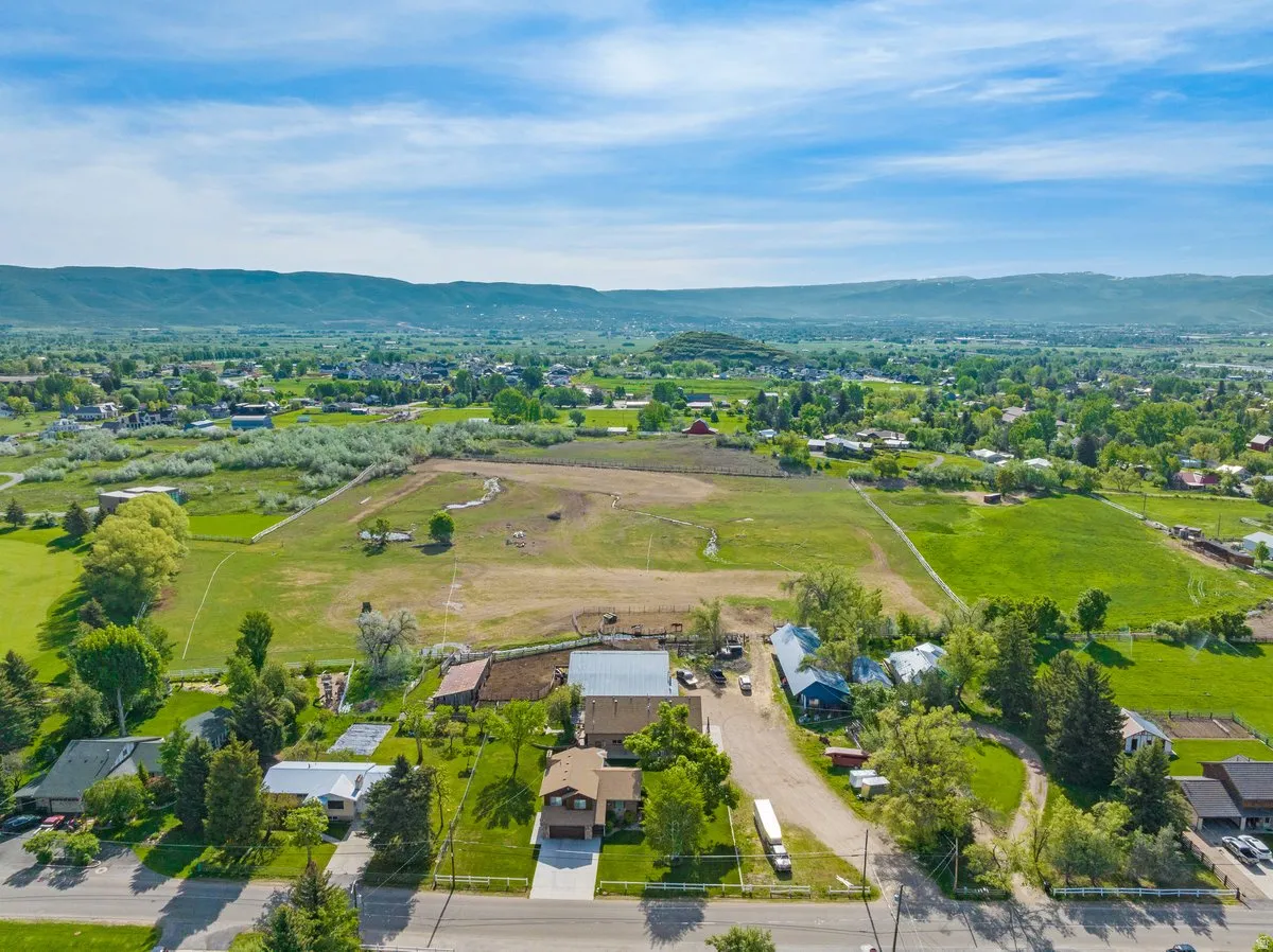 Aerial perspective showcasing the property's expansive green lawn and mature trees, surrounded by a rural landscape with agricultural fields and distant mountainous terrain