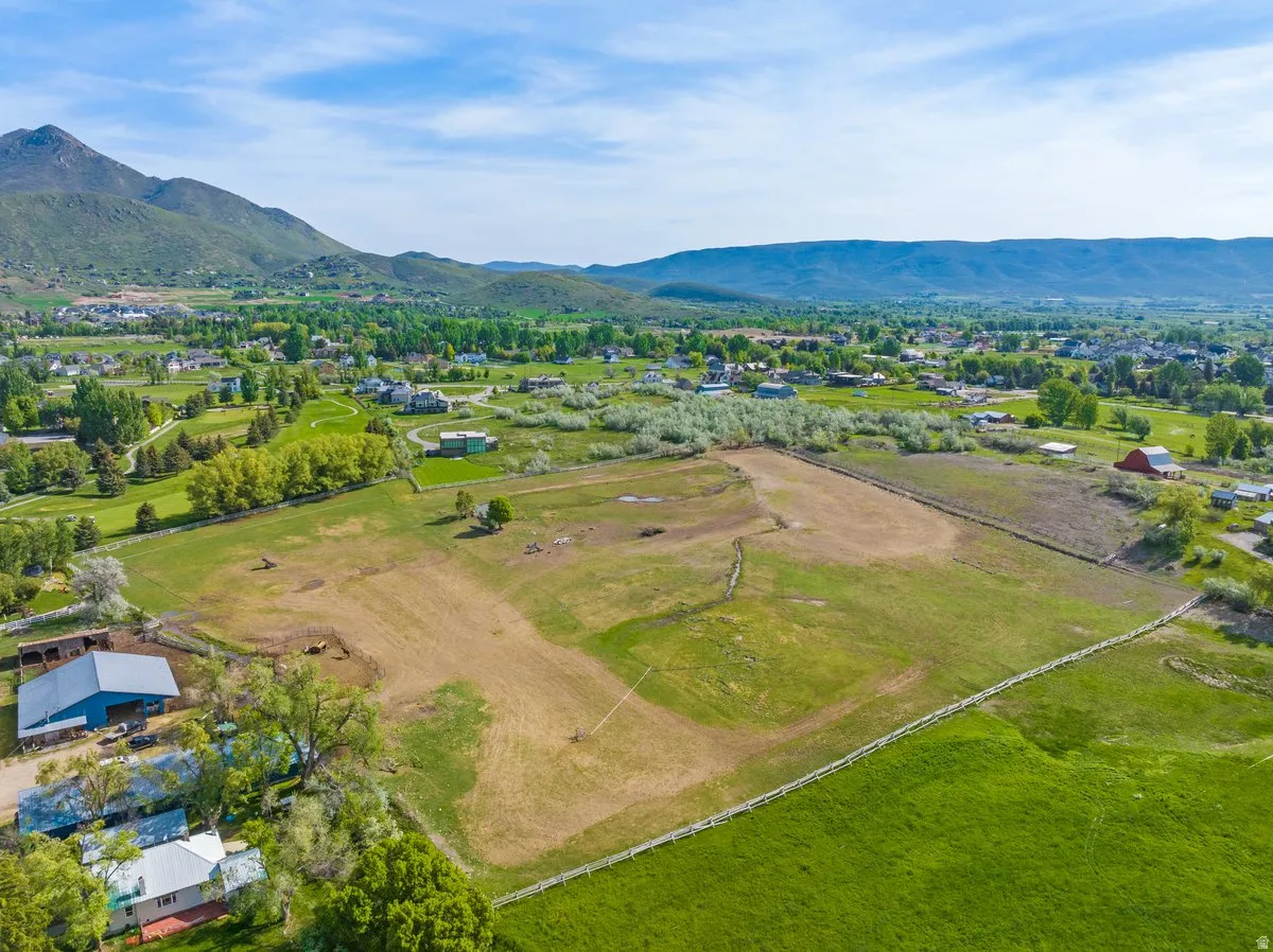 Expansive acreage featuring a white perimeter fence, mature trees, and mountainous terrain in the distance