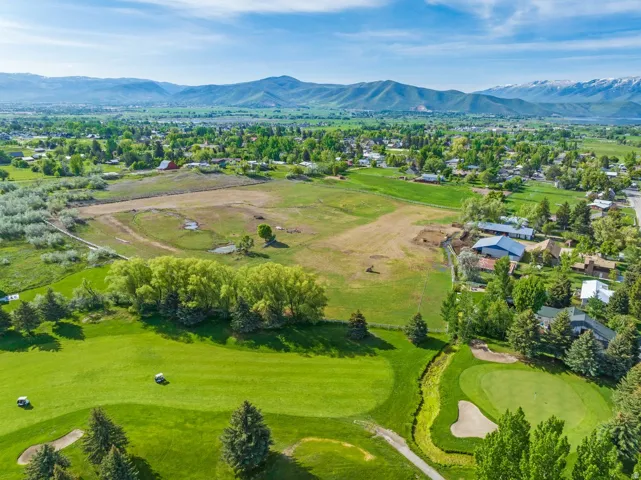 Expansive green landscape featuring a golf course, mature trees, and mountainous terrain in the distance