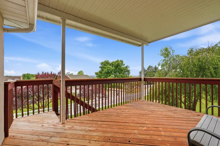 Spacious outdoor deck featuring natural wood-finish flooring, a covered patio, and stained wood railing with balusters