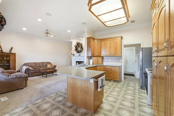 Open-concept kitchen and living area featuring wood-finish cabinetry, a central island with countertop seating, geometric pattern flooring, a fireplace with a mantel, and recessed lighting