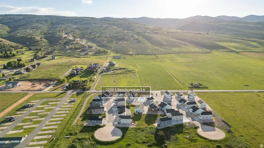 Aerial perspective showcasing a community of homes with paved access, surrounded by expansive green fields and distant mountains