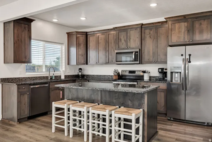 Kitchen featuring wood-finish flooring, dark wood cabinetry, granite countertops, and stainless steel appliances