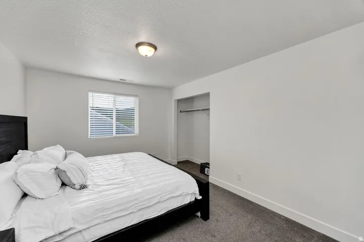 Bright bedroom with light gray walls, textured ceiling, and gray carpet flooring