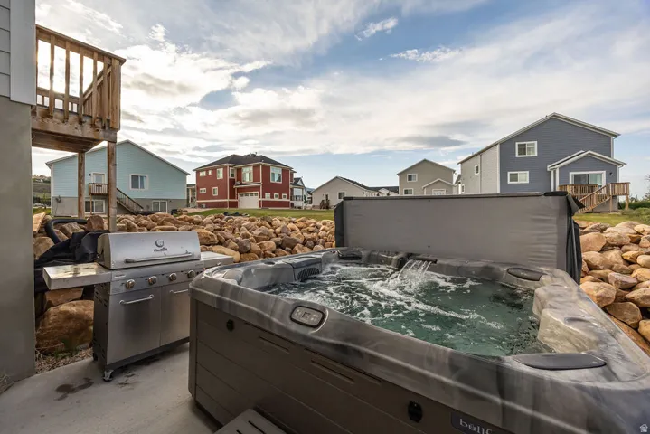 Outdoor patio featuring a built-in hot tub with waterfall feature, stainless steel grill, and natural rock landscaping