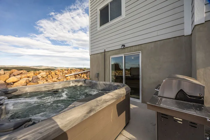 Outdoor hot tub with surrounding rock landscaping, a concrete patio, and sliding glass door access to the interior