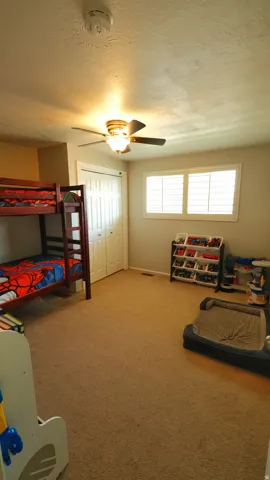 Carpeted room featuring a ceiling fan with integrated lighting, two windows with white plantation shutters, and a bi-fold closet door