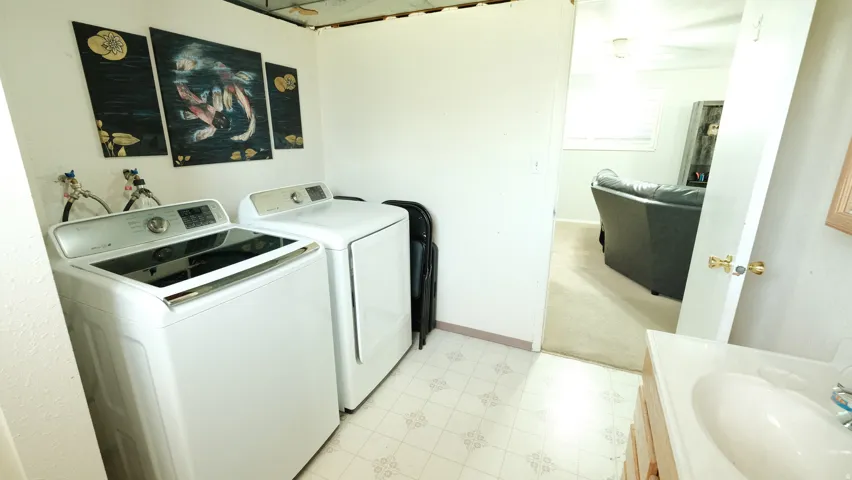 Dedicated laundry area featuring a white washer and dryer, patterned vinyl flooring, and direct access to an additional room with carpeting