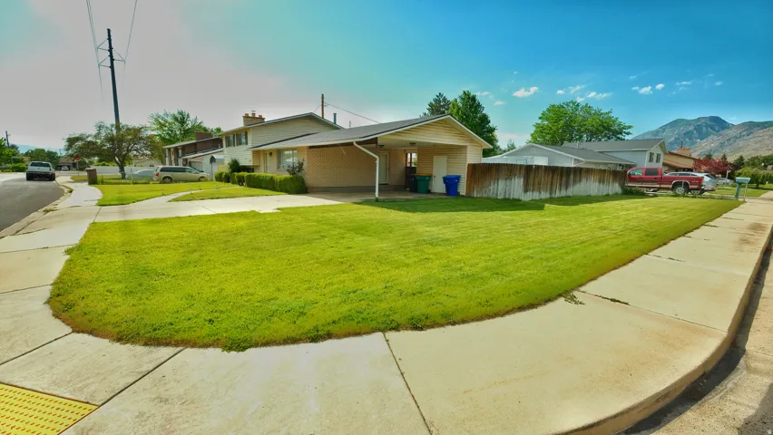 Corner lot residence featuring a spacious front lawn, concrete driveway, and a covered carport