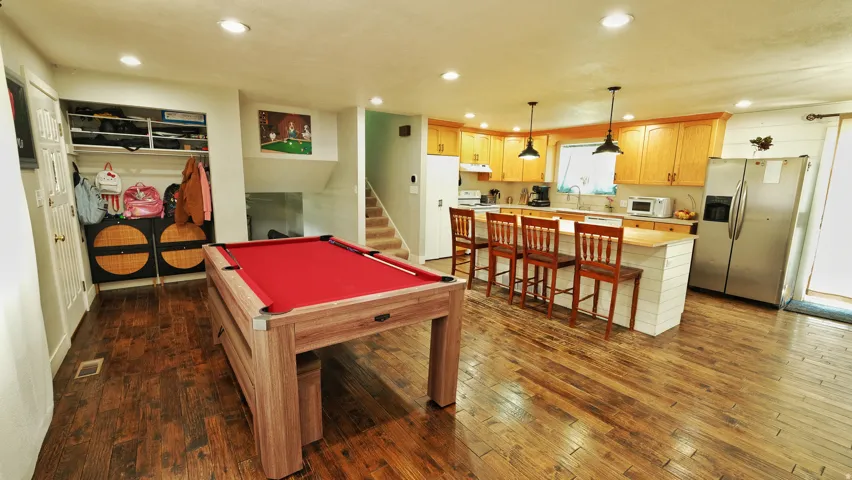 Spacious open-concept area featuring wide plank wood-finish flooring, a full kitchen with natural wood cabinetry and a central island with bar seating, and recessed lighting