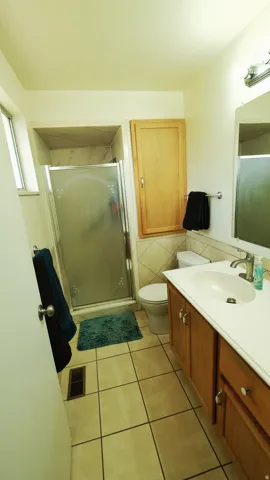 Bathroom featuring a glass-enclosed shower, white tile flooring, a single vanity with wood cabinetry, and a built-in wall cabinet for storage