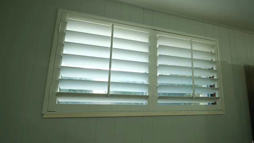 Window with white plantation shutters and light-colored vertical paneling