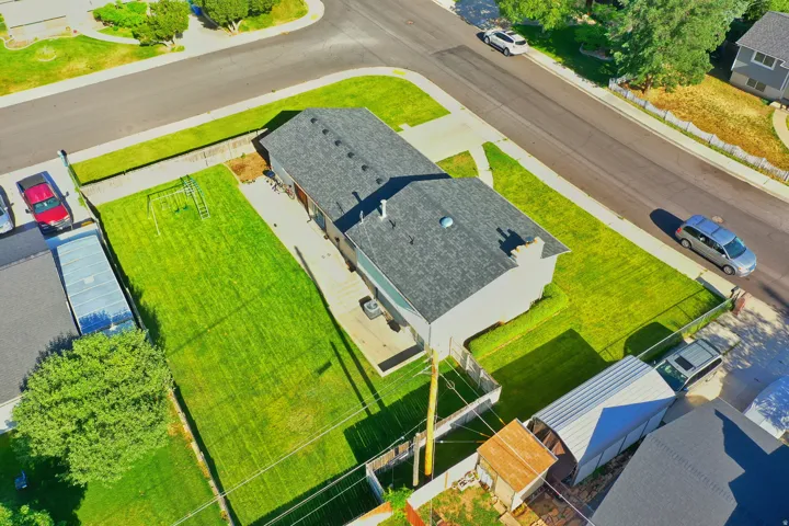 Aerial view showcasing a residential property with a shingle roof and a spacious, fenced backyard featuring a grassy lawn