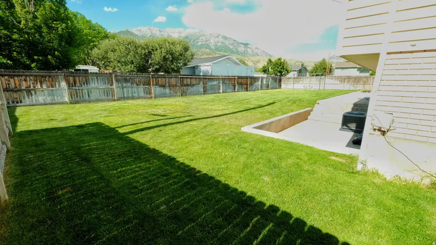 Expansive rear yard featuring a large grass lawn, perimeter fencing, and concrete patio area with integrated steps
