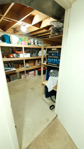 Concrete floor basement storage area with exposed wood joists and built-in shelving units
