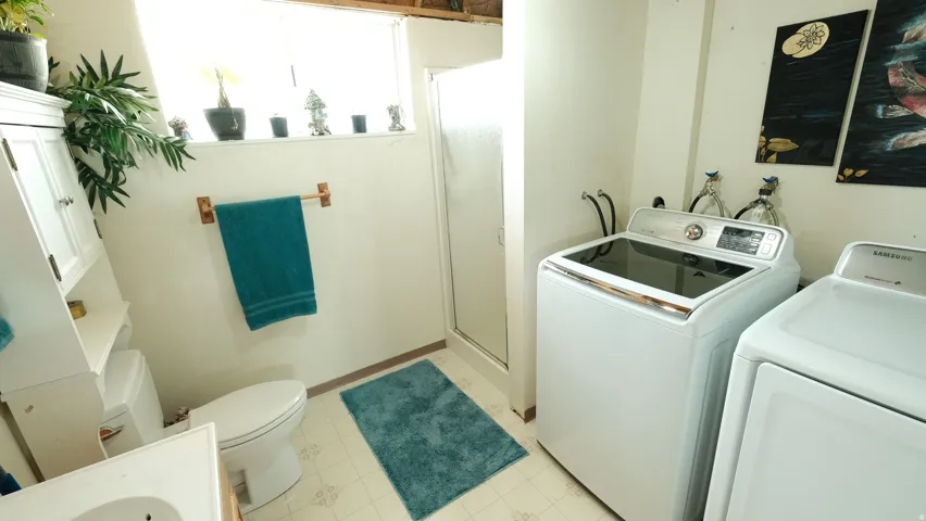 Utility space featuring a white toilet, white built-in storage cabinet, a glass-enclosed shower, and a high window