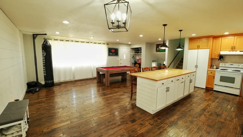 Open-concept living area featuring rich wood-finish flooring, recessed lighting, and a prominent kitchen island with a light-toned countertop