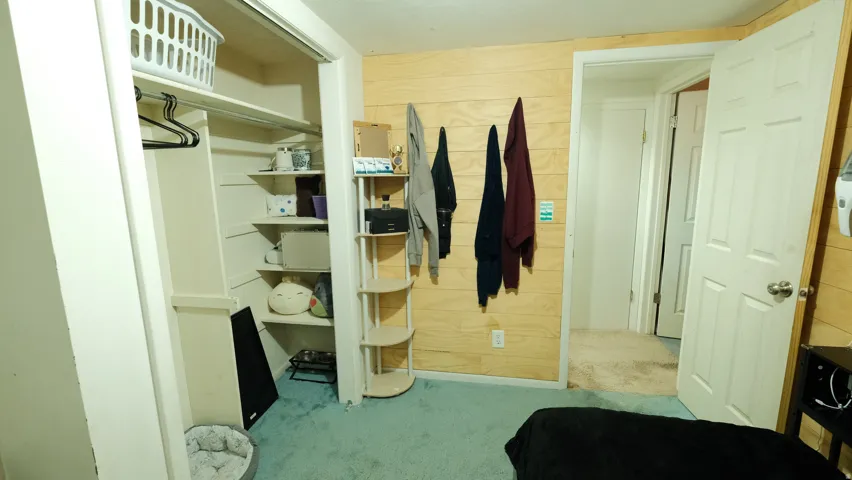 Built-in closet with shelving and hanging rod, complemented by wood-paneled walls and soft turquoise carpeting