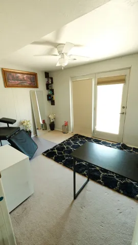 Room featuring a ceiling fan, light-colored carpeting, a door with a window, and an additional window with blinds