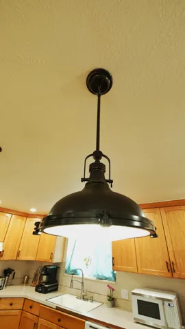Industrial-style pendant light illuminating a kitchen with wood cabinetry, light-toned countertops, and an undermount sink with a gooseneck faucet