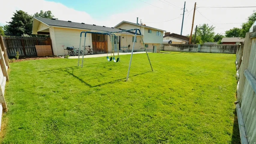 Expansive backyard featuring a large grass lawn, a wood fence perimeter, and a light-colored exterior wall with a covered patio area