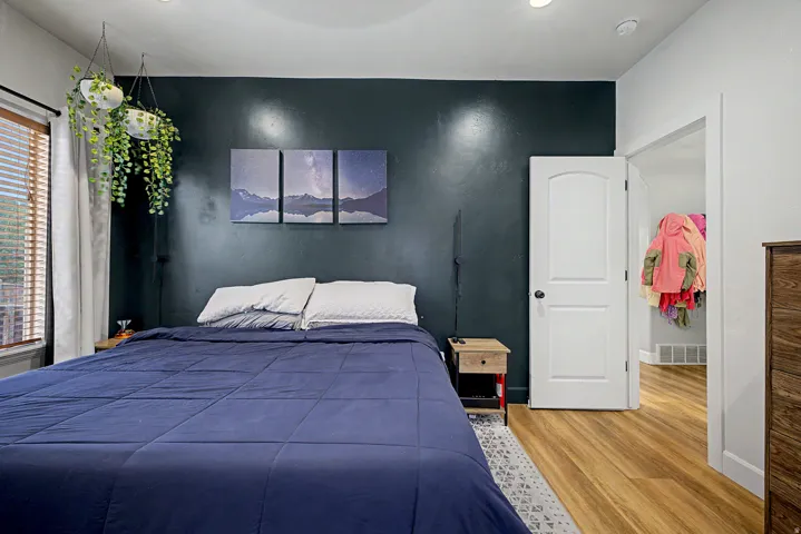 Bedroom featuring a contrasting accent wall, recessed lighting, wood-finish flooring, a window with blinds, and a white interior door