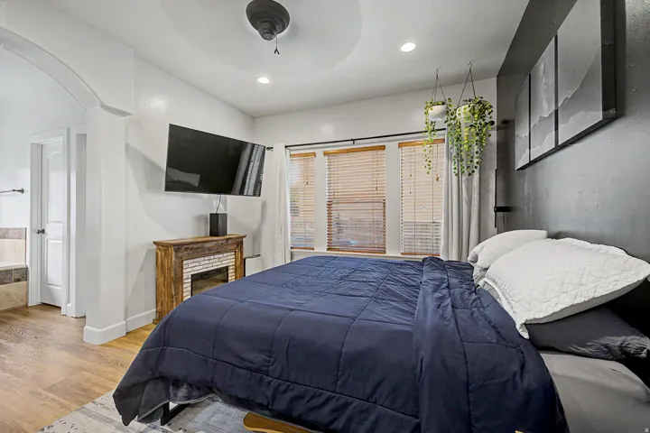 Spacious bedroom featuring wood-finish flooring, a decorative fireplace, recessed lighting, a ceiling fan, and multiple windows with blinds