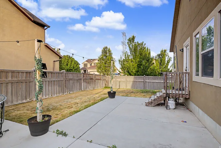 Spacious backyard with a large concrete patio, fenced perimeter, and a wooden staircase providing exterior access