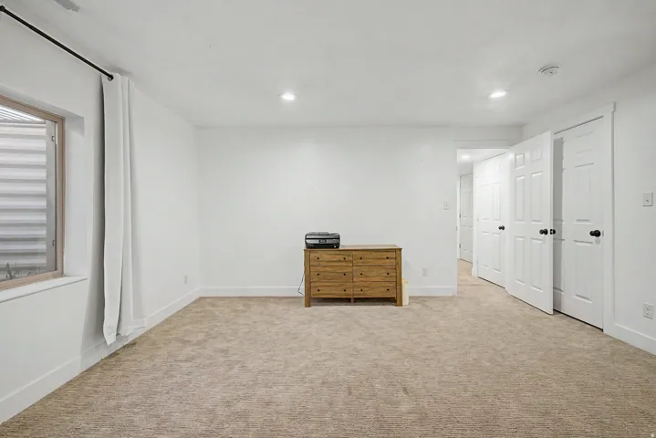 Spacious room featuring neutral carpeting, white walls, recessed lighting, and a white six-panel door