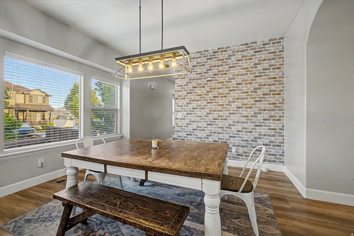 Dining area featuring a decorative brick-patterned accent wall, wood-finish flooring, and an arched entryway