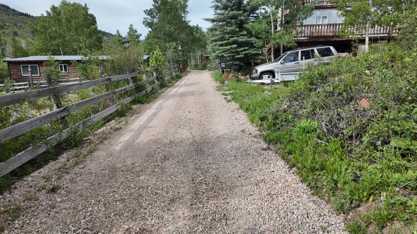 Gravel drive leading to a multi-level structure with a wood deck and surrounding mature trees