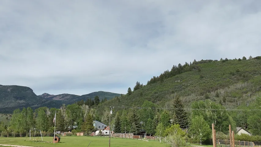Expansive green field with natural landscaping, surrounded by mature trees and distant mountain ranges