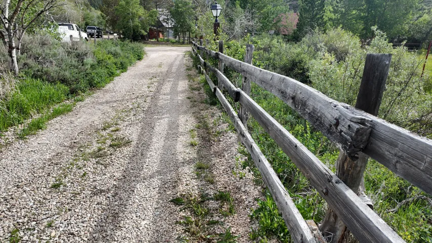 Gravel driveway bordered by a split-rail fence and abundant natural landscaping