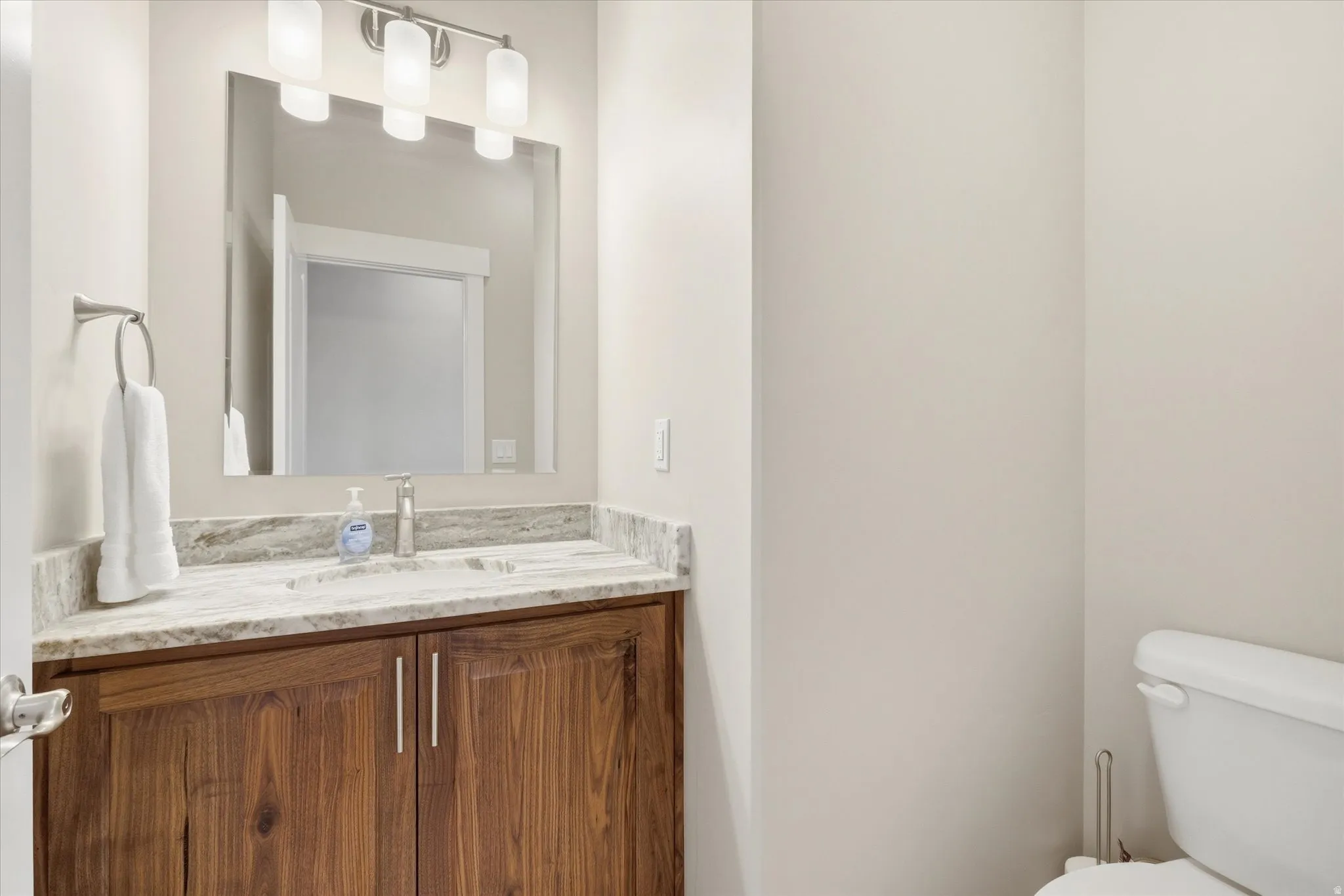 Vanity featuring wood-finish cabinetry, a stone countertop, an undermount sink, and a framed mirror with a modern light fixture
