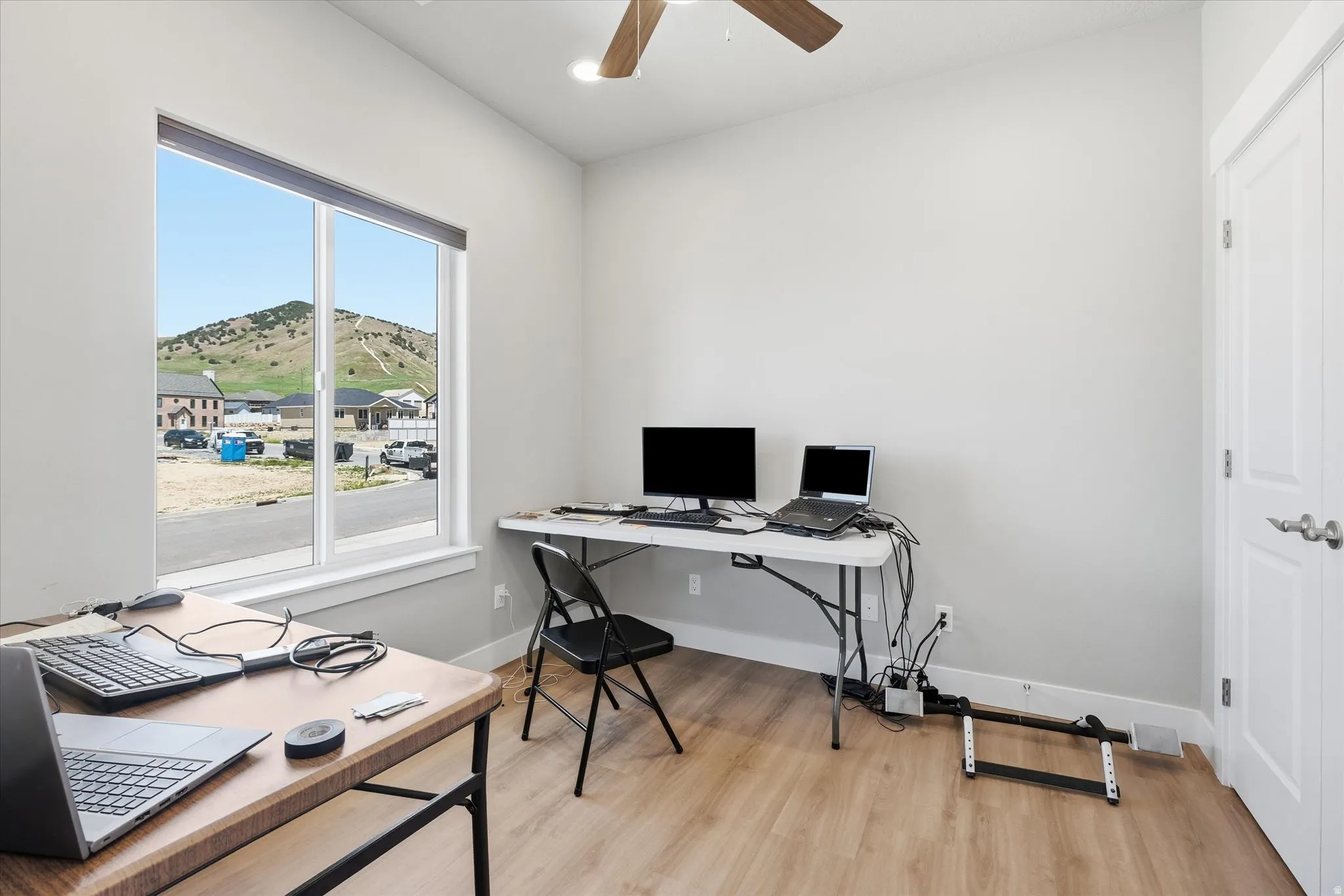 Room featuring wood-finish flooring, a ceiling fan, and a large window with white trim