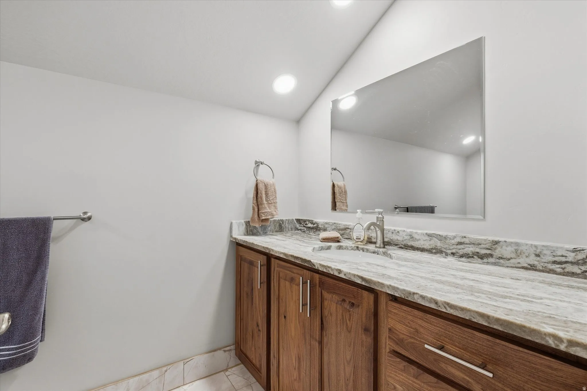 Bathroom vanity featuring a light-toned stone countertop with an integrated sink, wood-finish cabinetry, and a rectangular mirror