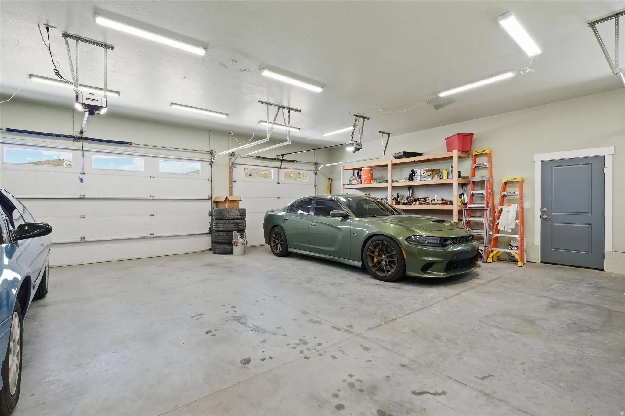 Spacious garage featuring two overhead doors with window panels, multiple fluorescent lighting fixtures, and a side access door