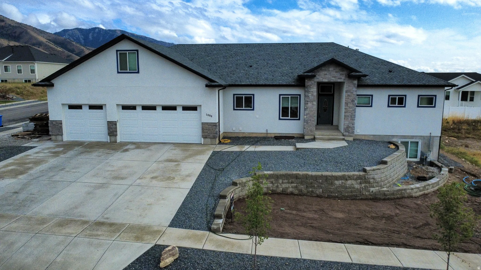 White stucco exterior with stone accents, a concrete driveway, a two-car garage, and a retaining wall