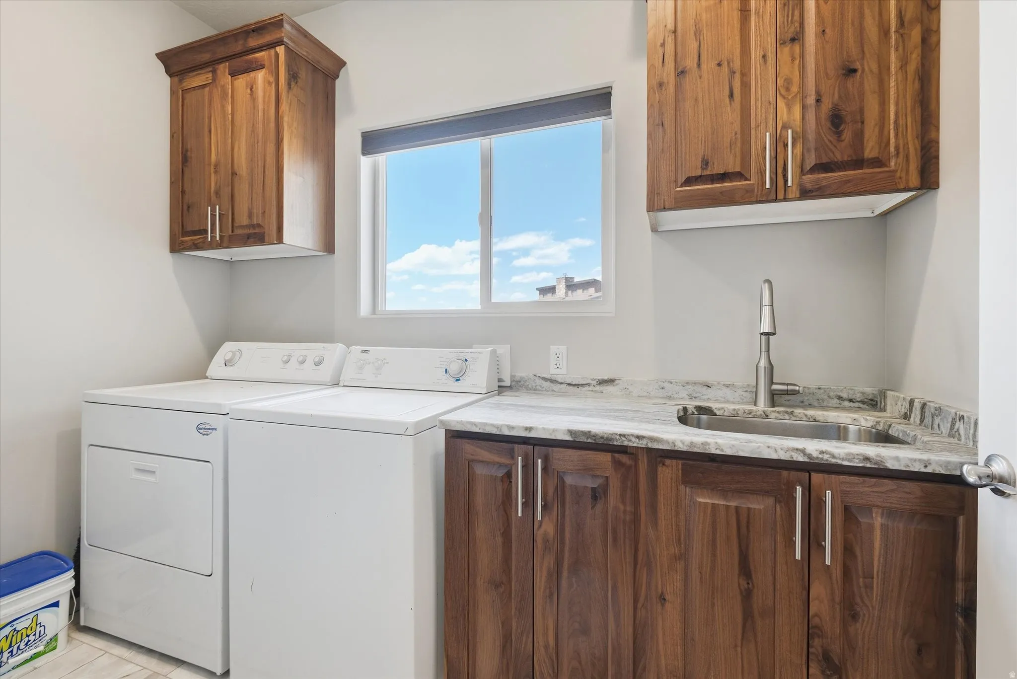 Functional laundry room featuring a utility sink, wood-finish cabinetry, and solid surface countertops