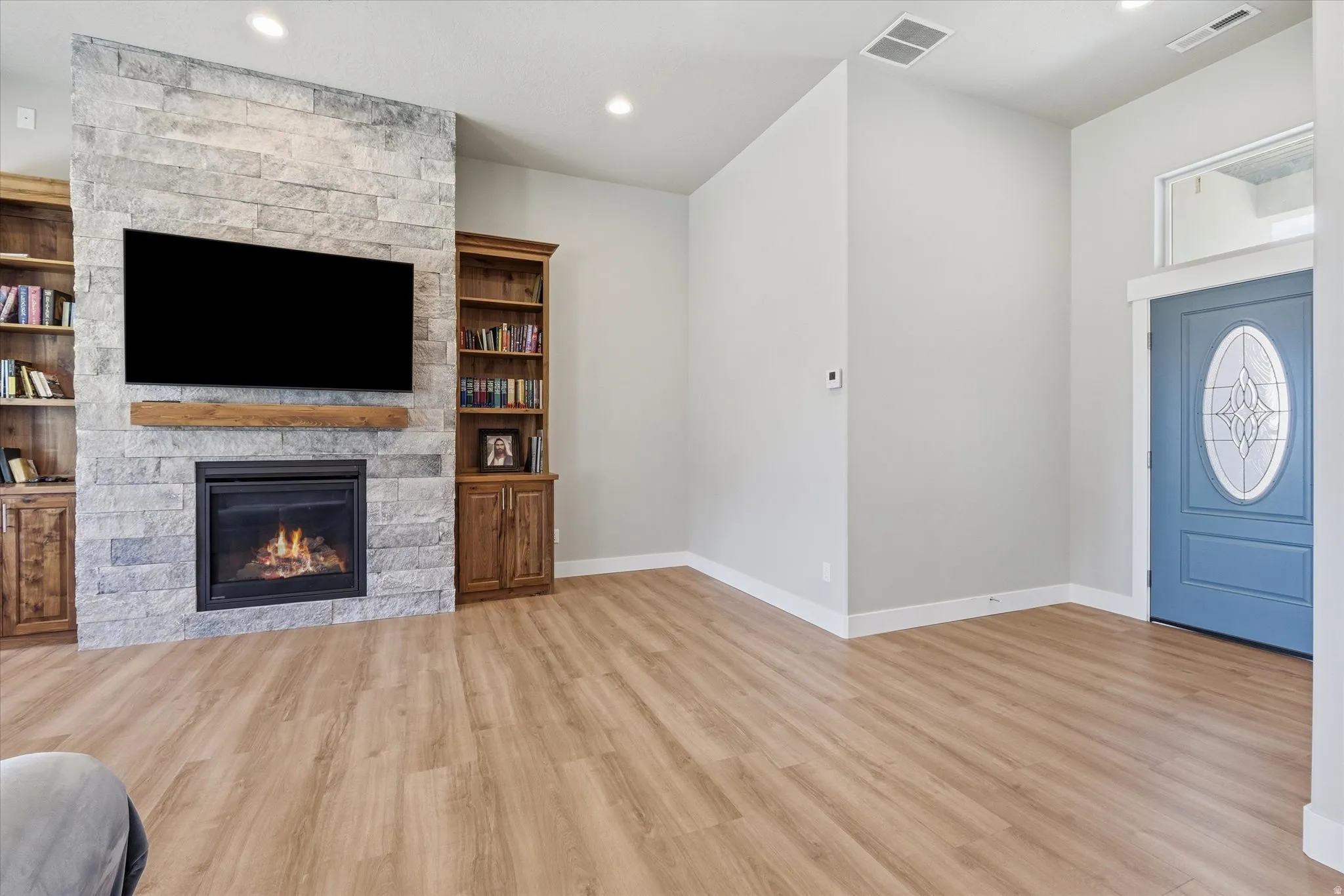 Living space featuring a stone-clad fireplace with a wood mantel, built-in wooden shelving, wood-finish flooring, and a blue entry door with decorative glass