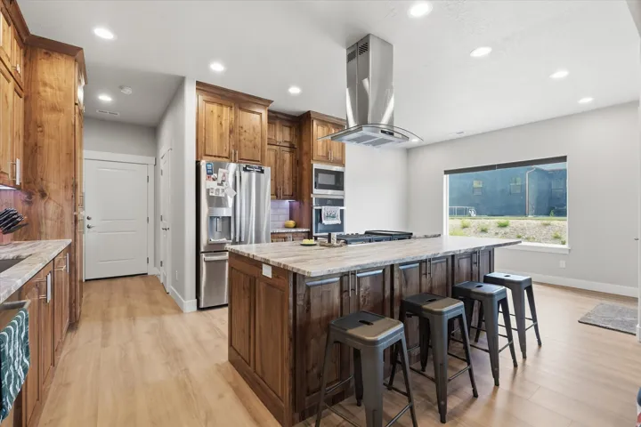 Spacious kitchen featuring an expansive central island with seating, wood-finish cabinetry, stainless steel appliances, and light wood-finish flooring