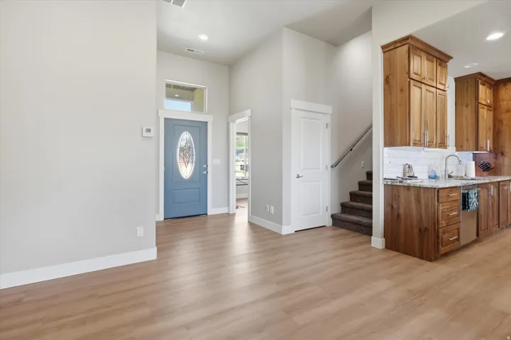 Open-concept living area with wood-finish flooring, a contemporary blue entry door with decorative glass, and a kitchen featuring wood cabinetry, light-toned countertops, and a subway tile backsplash