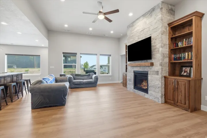 Spacious living area featuring a stone-clad fireplace with wood mantle, built-in shelving, wood-finish flooring, and recessed lighting