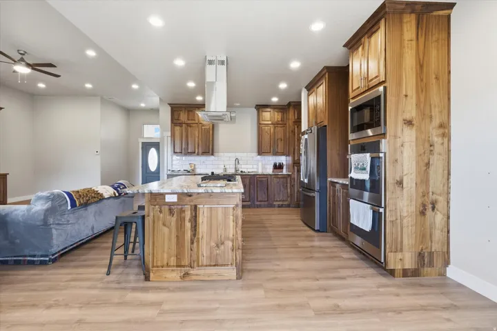 Kitchen featuring wood cabinetry, stainless steel appliances, a center island with a stone countertop, and wood-finish flooring