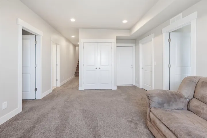 Spacious interior room featuring light gray walls, white trim, recessed lighting, and neutral carpeting